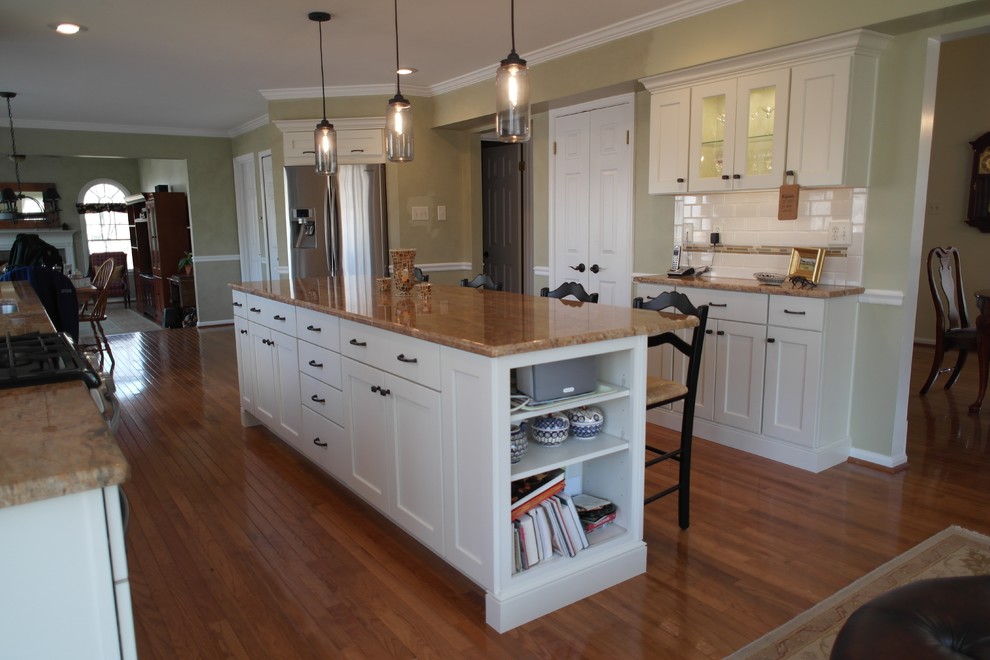 Mid-sized transitional u-shaped open plan kitchen in Baltimore with an undermount sink, recessed-panel cabinets, white cabinets, granite benchtops, white splashback, subway tile splashback, stainless steel appliances, medium hardwood floors, with island and brown floor.
