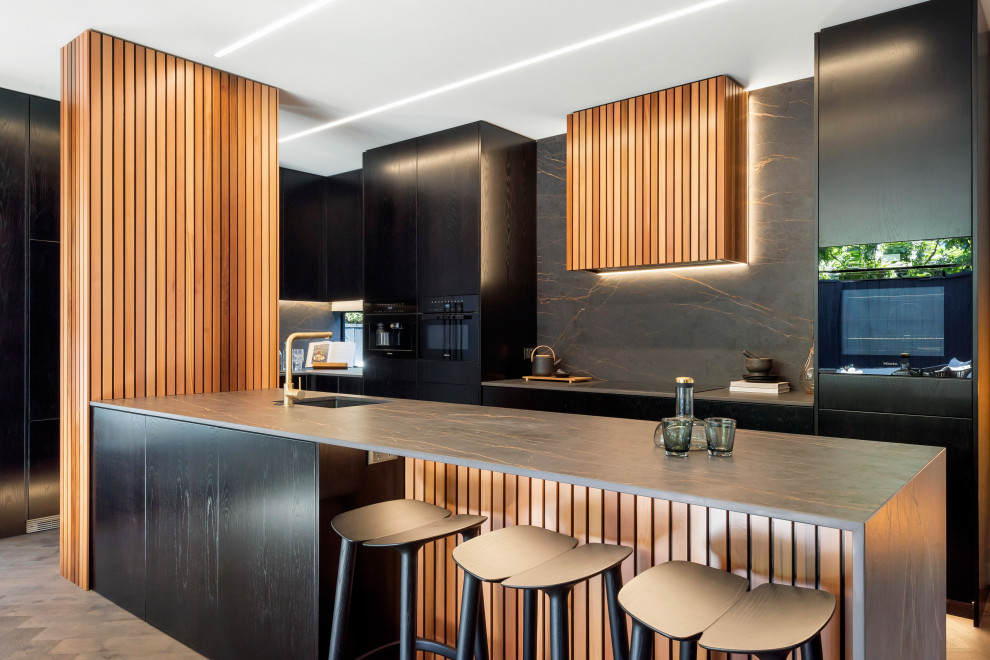 This is an example of a medium sized contemporary u-shaped kitchen/diner in Auckland with a submerged sink, flat-panel cabinets, black cabinets, composite countertops, black splashback, porcelain splashback, black appliances, dark hardwood flooring, an island, brown floors and black worktops.