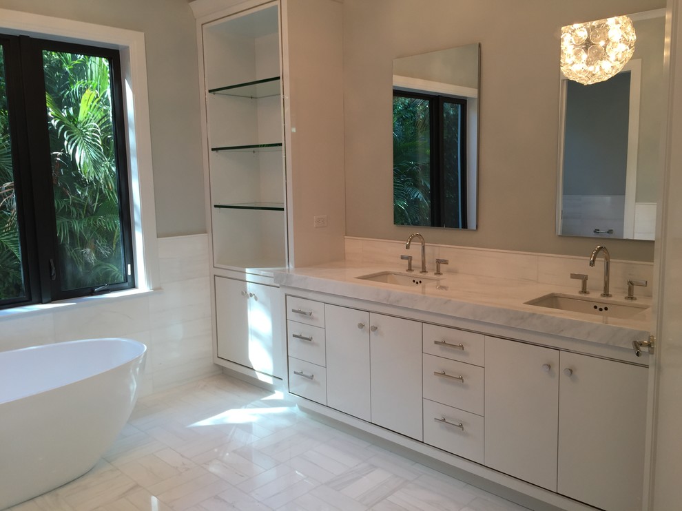 Inspiration for a mid-sized contemporary master bathroom in Miami with recessed-panel cabinets, white cabinets, a freestanding tub, a curbless shower, a one-piece toilet, white tile, porcelain tile, grey walls and marble floors.
