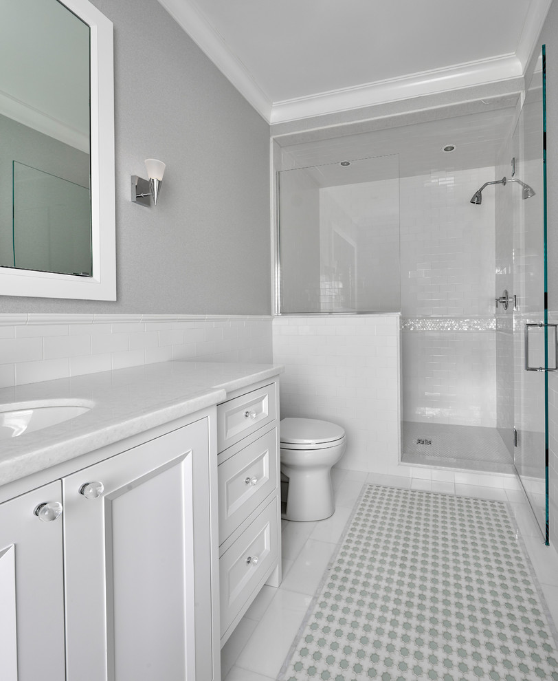 Design ideas for a mid-sized modern bathroom in Chicago with recessed-panel cabinets, white cabinets, an alcove shower, a two-piece toilet, white tile, subway tile, grey walls, ceramic floors, an undermount sink, marble benchtops, multi-coloured floor, a hinged shower door and white benchtops.