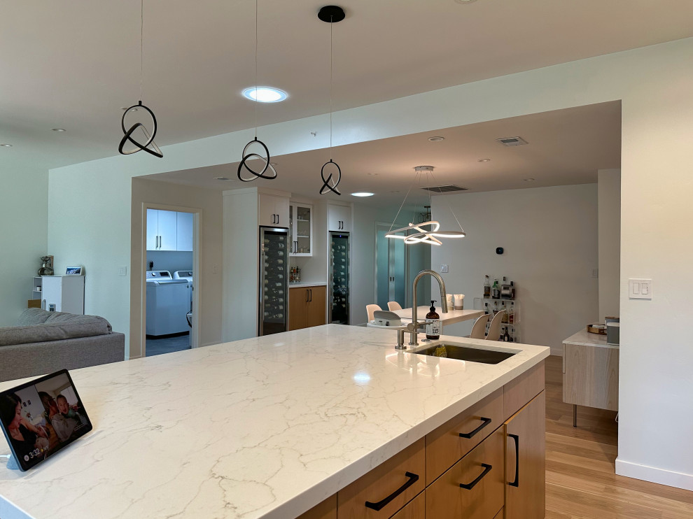 Design ideas for a large modern l-shaped kitchen in San Francisco with an undermount sink, flat-panel cabinets, white cabinets, quartz benchtops, white splashback, subway tile splashback, stainless steel appliances, light hardwood floors, with island, brown floor and white benchtop.