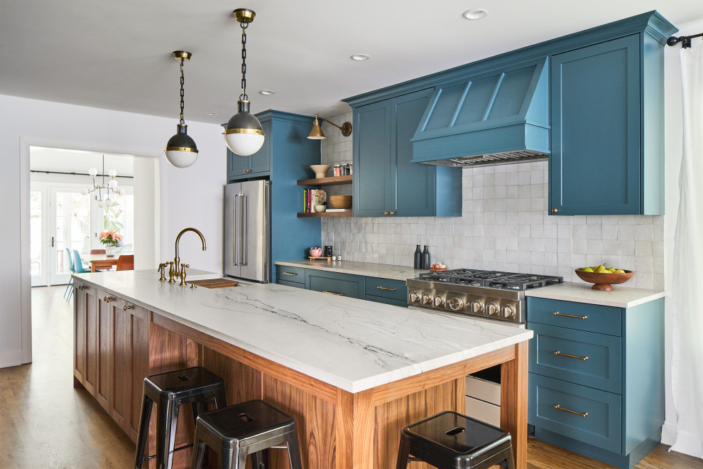 Design ideas for a mid-sized transitional galley kitchen in Austin with shaker cabinets, blue cabinets, medium hardwood floors, with island, a farmhouse sink, white splashback, stainless steel appliances, brown floor and white benchtop.