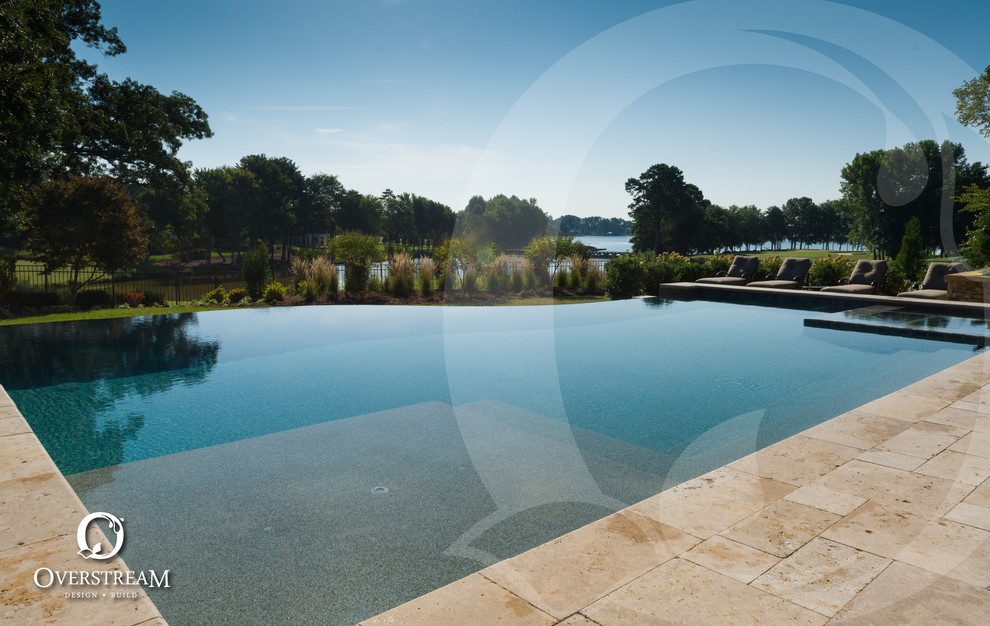 This is an example of a large modern backyard custom-shaped infinity pool in Charlotte with a hot tub and natural stone pavers.