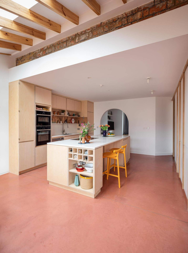 Foto de cocina actual grande abierta con armarios con paneles lisos, puertas de armario de madera clara, suelo de cemento, una isla y suelo rosa