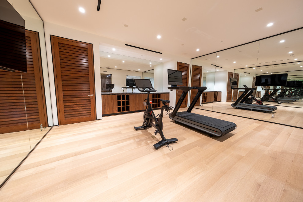 Home weight room - large medium tone wood floor and brown floor home weight room idea in Los Angeles with white walls