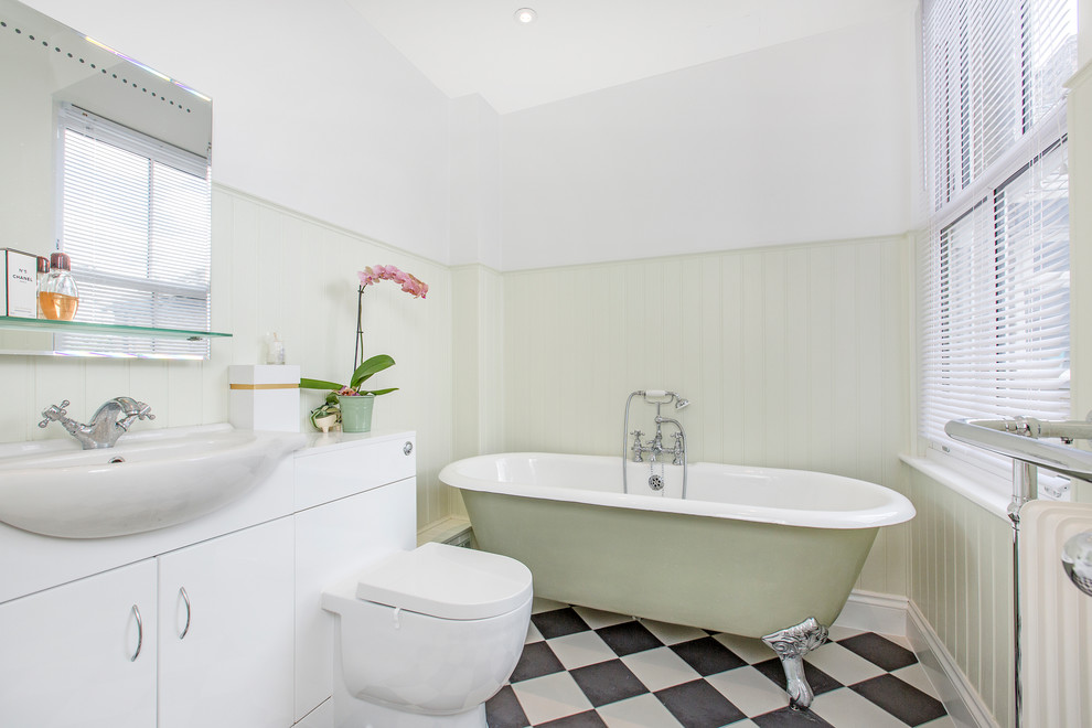 Photo of a small transitional master bathroom in London with flat-panel cabinets, white cabinets, a claw-foot tub, a wall-mount toilet, black and white tile, white walls and a drop-in sink.