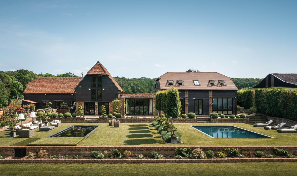 Стильный дизайн: большой, трехэтажный, черный частный загородный дом в современном стиле с двускатной крышей и коричневой крышей - последний тренд