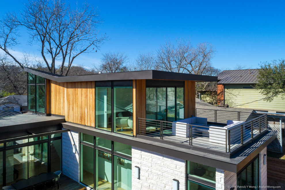Photo of a mid-sized midcentury two-storey white house exterior in Austin with stone veneer and a metal roof.