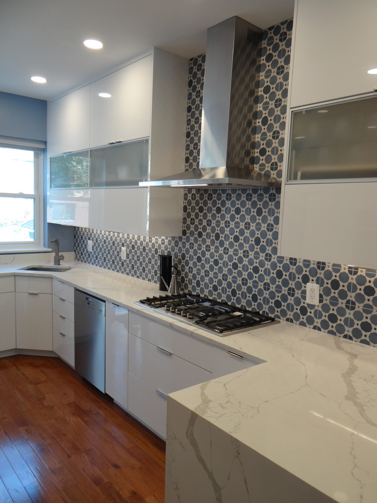 Photo of a small modern galley separate kitchen in DC Metro with an undermount sink, flat-panel cabinets, white cabinets, quartz benchtops, blue splashback, cement tile splashback, stainless steel appliances, medium hardwood floors, a peninsula, orange floor and white benchtop.