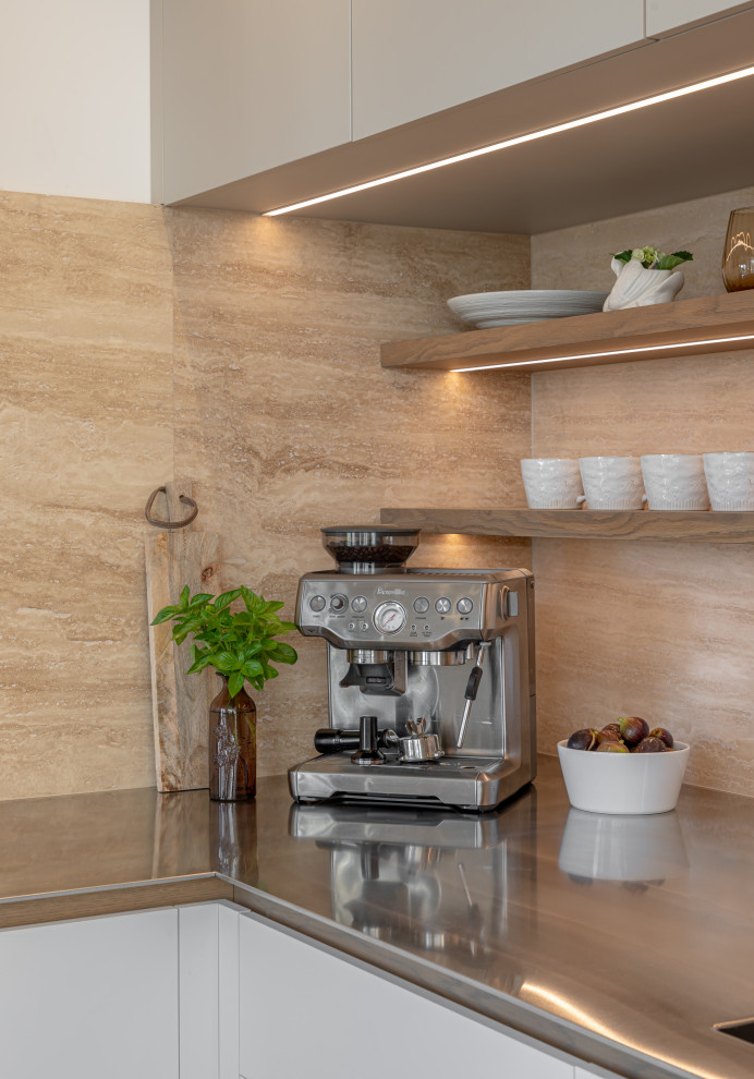 This is an example of a medium sized modern u-shaped kitchen/diner in Other with an integrated sink, flat-panel cabinets, beige cabinets, stainless steel worktops, beige splashback, travertine splashback, black appliances, light hardwood flooring, a breakfast bar and beige floors.