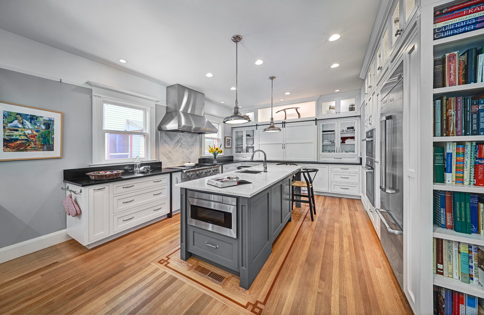 This is an example of a large traditional u-shaped open plan kitchen in Sacramento with an undermount sink, recessed-panel cabinets, white cabinets, soapstone benchtops, white splashback, marble splashback, stainless steel appliances, medium hardwood floors, with island, beige floor and black benchtop.