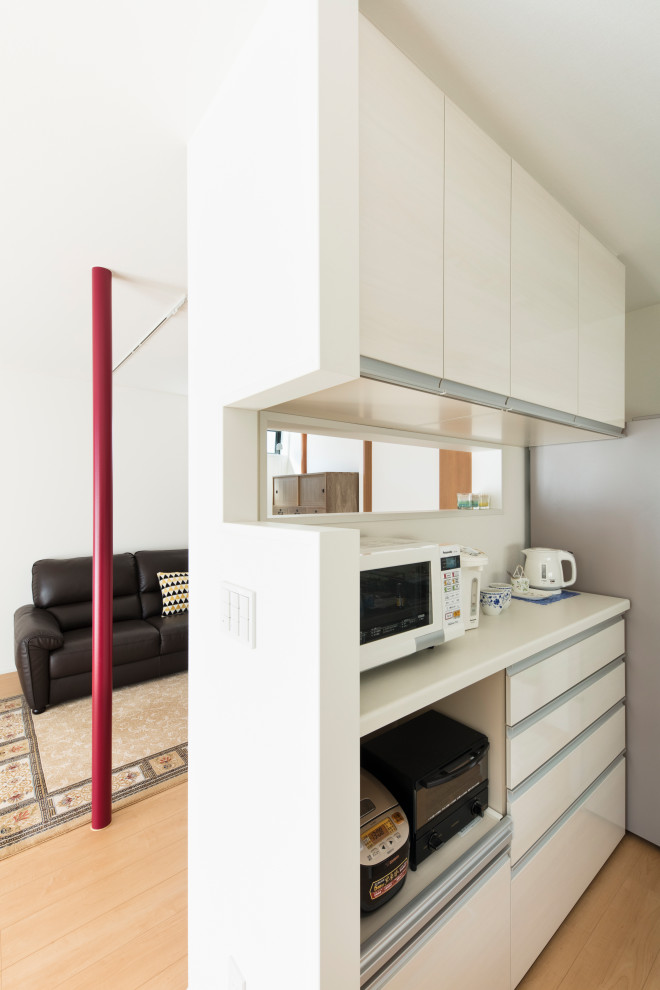 This is an example of a mid-sized modern galley eat-in kitchen in Tokyo with an integrated sink, flat-panel cabinets, white cabinets, solid surface benchtops, white splashback, plywood floors, white floor, white benchtop and timber.