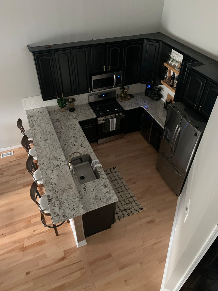 Design ideas for a mid-sized industrial u-shaped eat-in kitchen in Detroit with an undermount sink, raised-panel cabinets, black cabinets, granite benchtops, white splashback, mosaic tile splashback, stainless steel appliances, light hardwood floors, multi-coloured benchtop and vaulted.