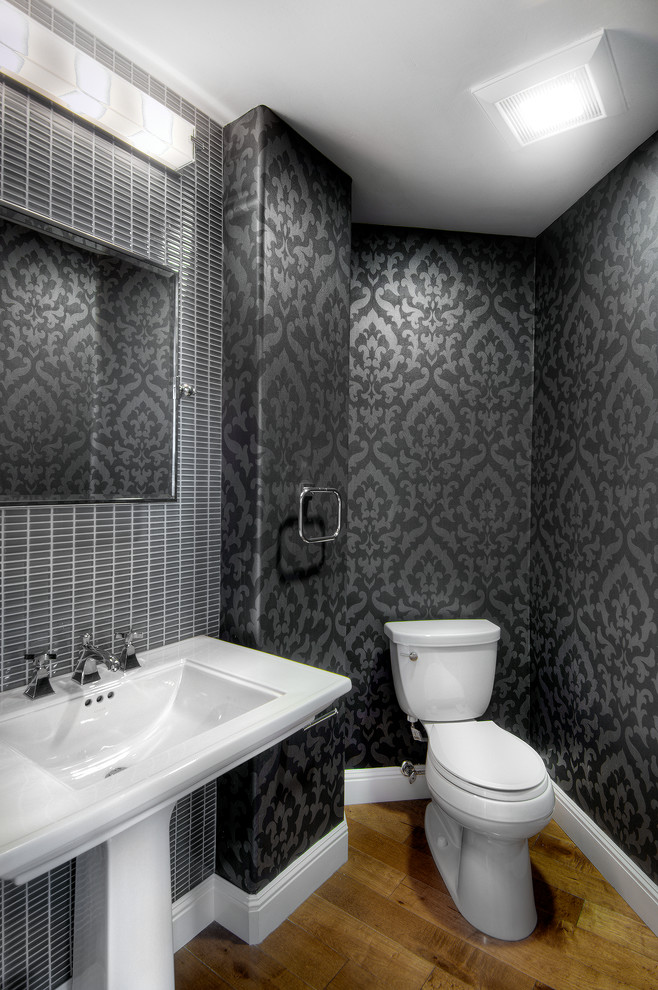 This is an example of a mid-sized transitional powder room in San Francisco with a pedestal sink, a two-piece toilet, gray tile, black walls and medium hardwood floors.