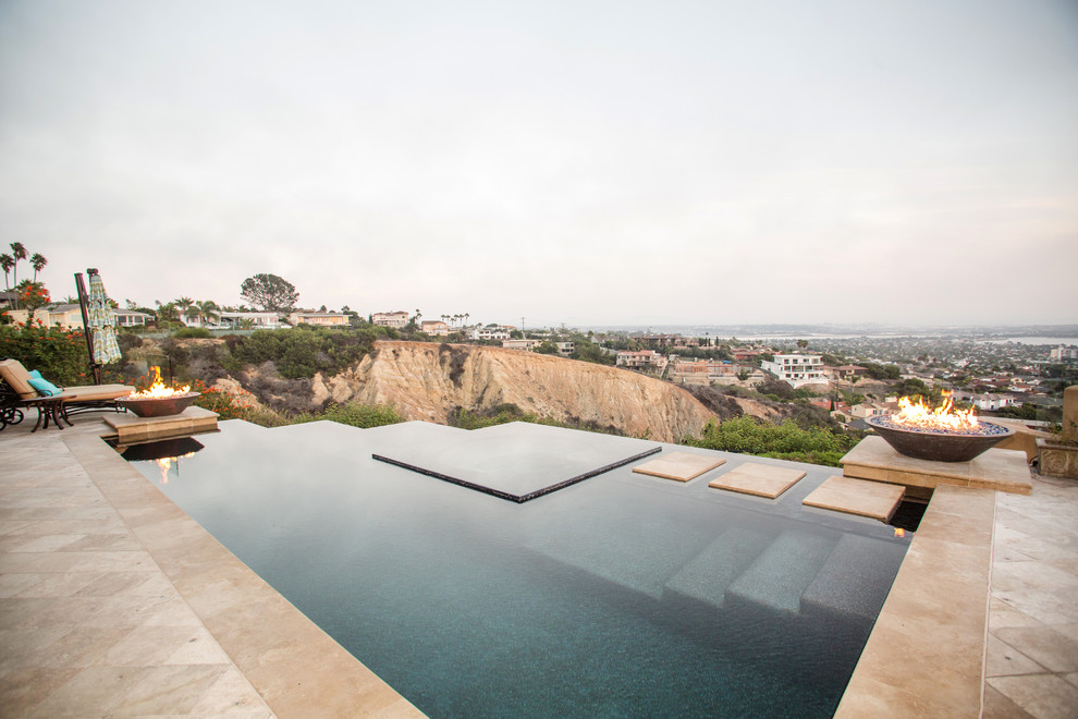 Photo of a large mediterranean backyard custom-shaped infinity pool in San Diego with natural stone pavers.