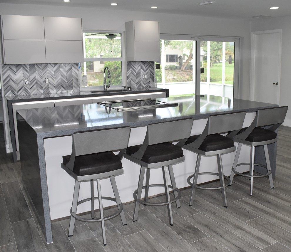 Design ideas for a mid-sized contemporary galley open plan kitchen in Miami with flat-panel cabinets, grey cabinets, solid surface benchtops, grey splashback, stainless steel appliances, with island, grey benchtop, an undermount sink, porcelain floors and grey floor.