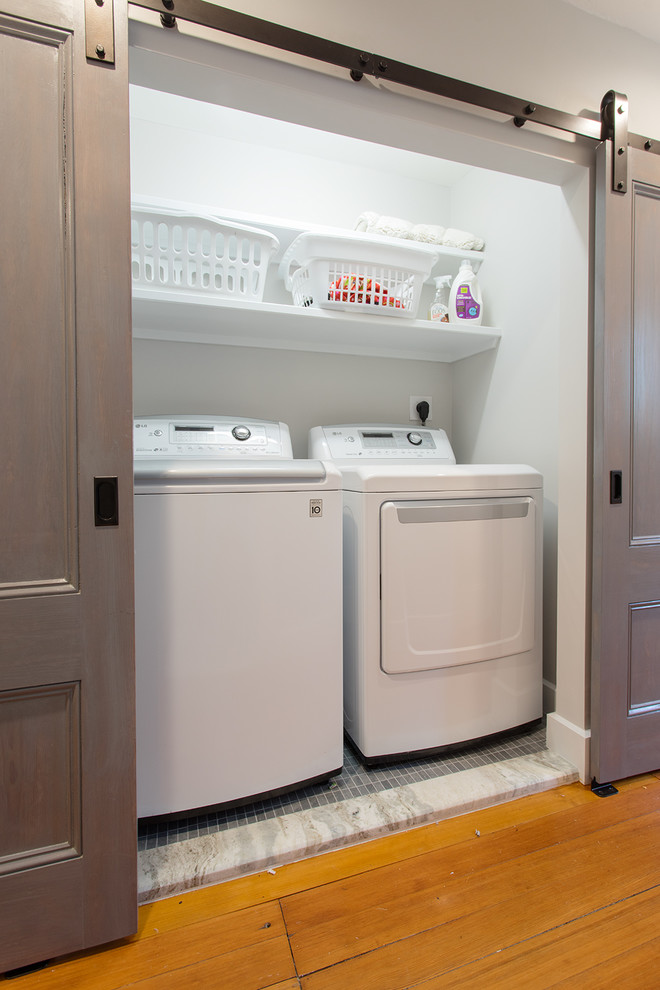 Photo of a small contemporary single-wall laundry cupboard in Boston with white walls, ceramic floors and a side-by-side washer and dryer.