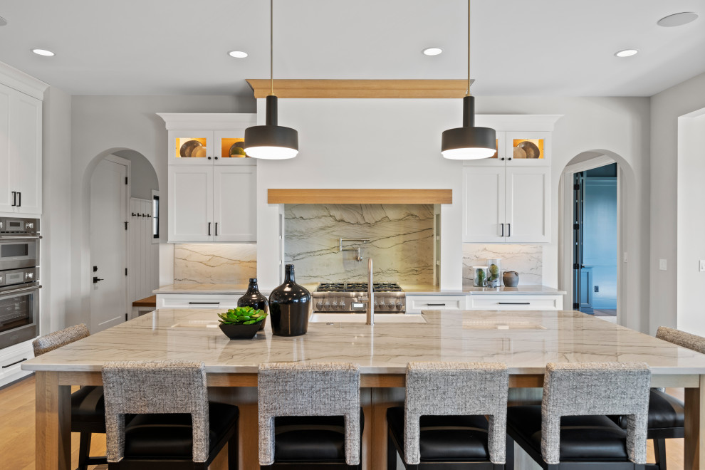 Transitional l-shaped medium tone wood floor and brown floor kitchen photo in Cincinnati with a farmhouse sink, recessed-panel cabinets, white cabinets, gray backsplash, stone slab backsplash, stainless steel appliances, an island and gray countertops