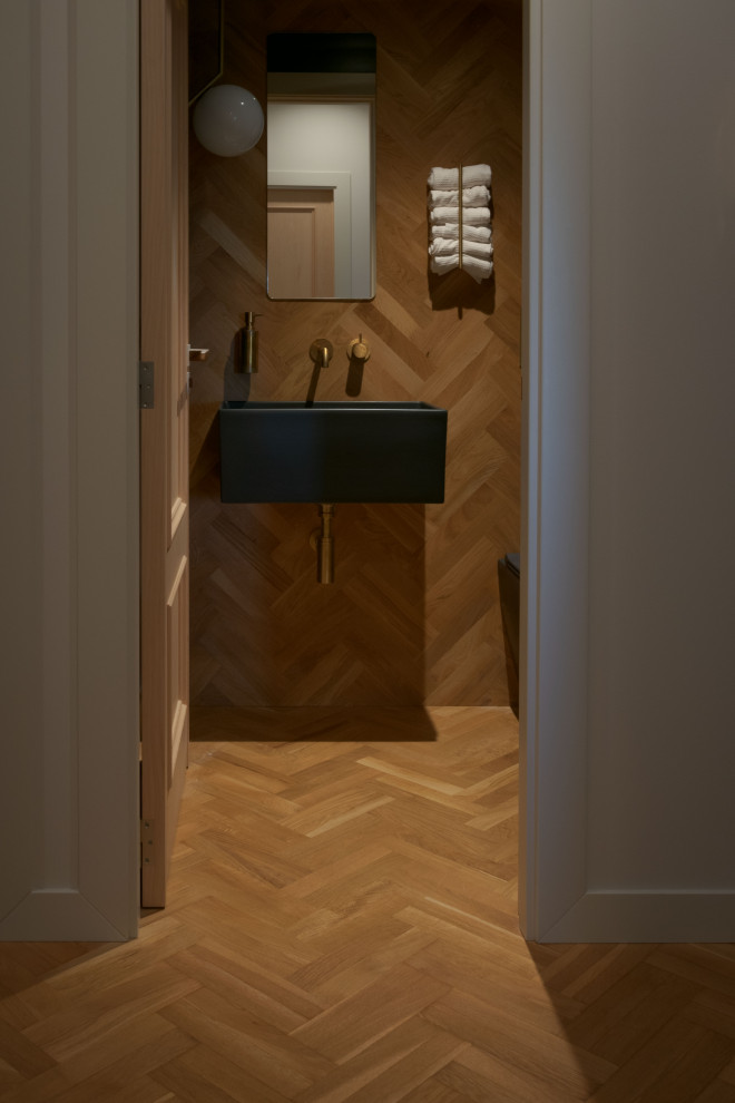 Cette image montre un petit WC et toilettes bohème en bois avec des portes de placard noires, WC à poser, un mur multicolore, un sol en bois brun, un lavabo suspendu et meuble-lavabo suspendu.