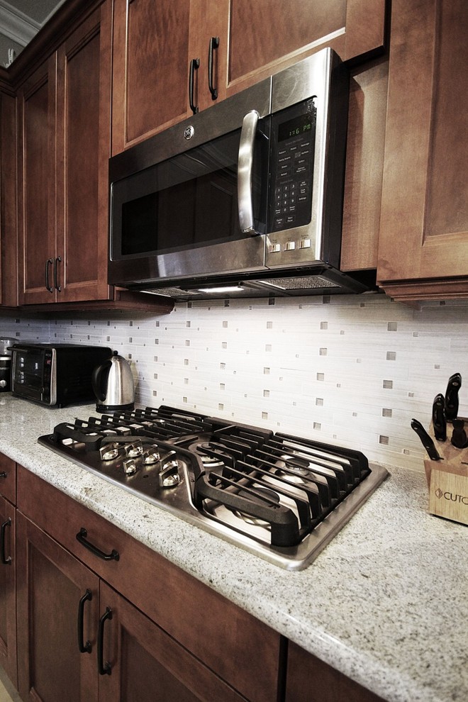 Example of a mid-sized transitional ceramic tile and beige floor eat-in kitchen design with a single-bowl sink, shaker cabinets, brown cabinets, granite countertops, white backsplash, stainless steel appliances, an island, white countertops and glass tile backsplash
