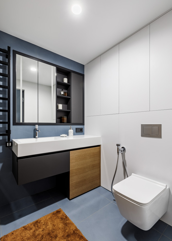 Пример оригинального дизайна: главная ванная комната среднего размера в современном стиле с плоскими фасадами, фасадами цвета дерева среднего тона, полновстраиваемой ванной, душем над ванной, инсталляцией, синей плиткой, керамической плиткой, коричневыми стенами, полом из керамической плитки, накладной раковиной, столешницей из искусственного камня, синим полом, душем с раздвижными дверями, белой столешницей, тумбой под одну раковину и напольной тумбой