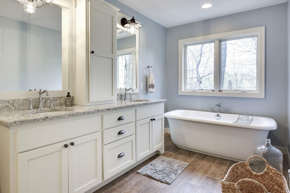 This is an example of a mid-sized country master bathroom in Minneapolis with recessed-panel cabinets, white cabinets, a freestanding tub, an open shower, white tile, ceramic tile, blue walls, ceramic floors, an undermount sink, granite benchtops, an open shower, brown floor and grey benchtops.