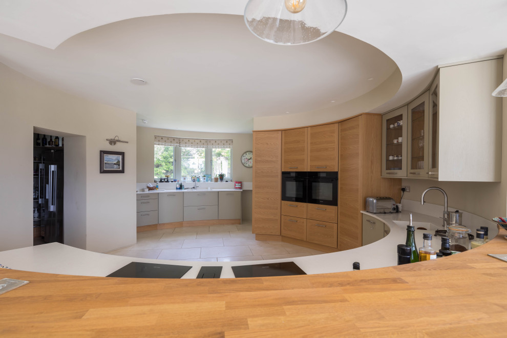Inspiration for a large contemporary kitchen in Cornwall with a built-in sink, flat-panel cabinets, medium wood cabinets, beige splashback, black appliances, limestone flooring, a breakfast bar, beige floors and beige worktops.