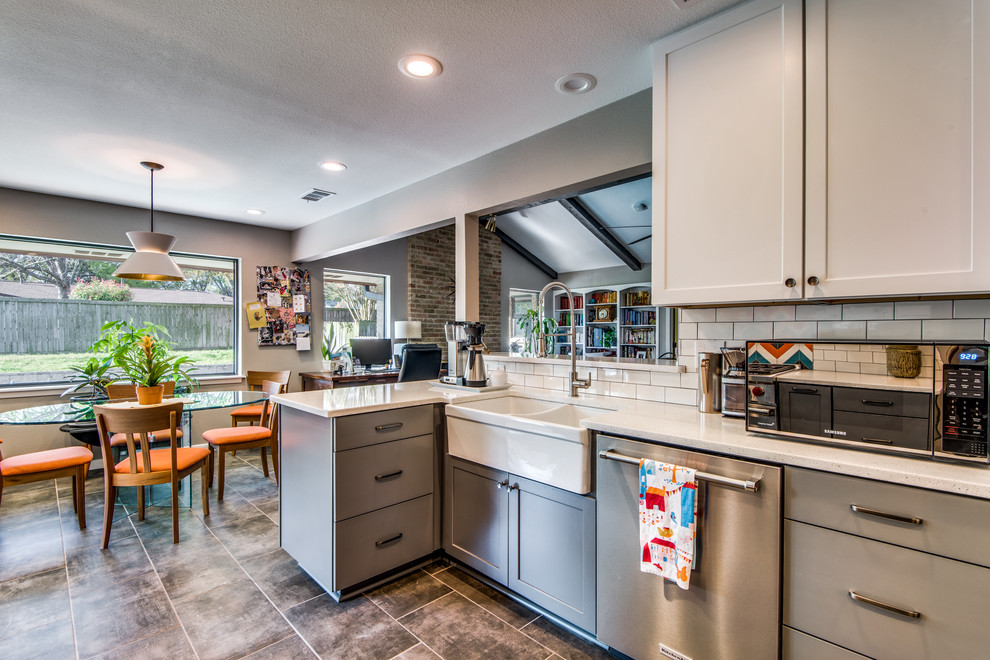Mid-sized modern u-shaped open plan kitchen in Austin with a farmhouse sink, shaker cabinets, grey cabinets, quartz benchtops, white splashback, subway tile splashback, stainless steel appliances, porcelain floors, a peninsula, brown floor and white benchtop.