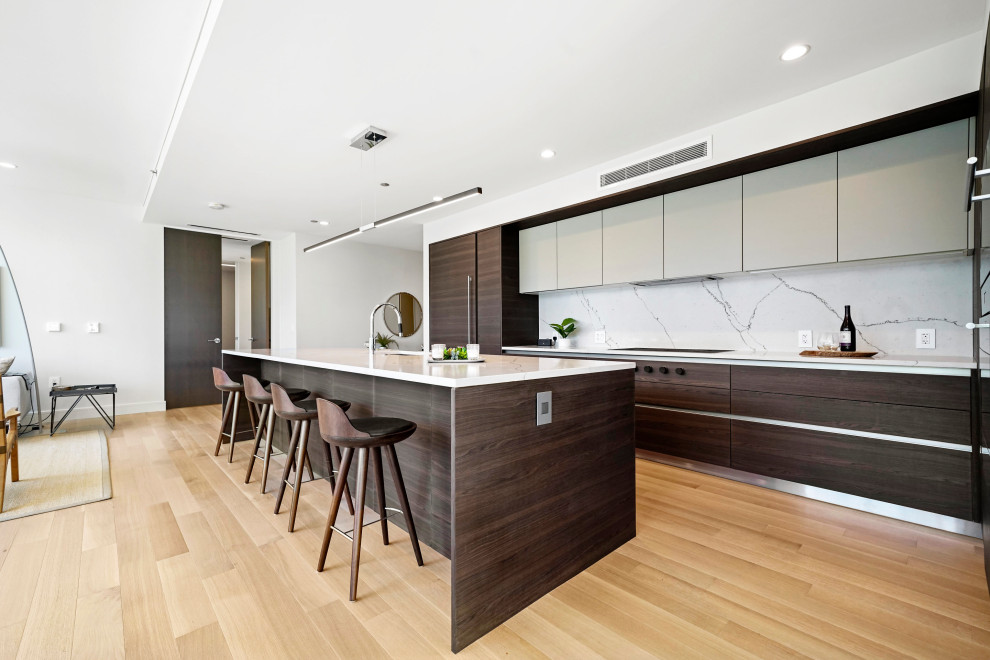 Inspiration for a contemporary l-shaped kitchen in Chicago with flat-panel cabinets, an undermount sink, dark wood cabinets, white splashback, panelled appliances, medium hardwood floors, with island, brown floor and white benchtop.