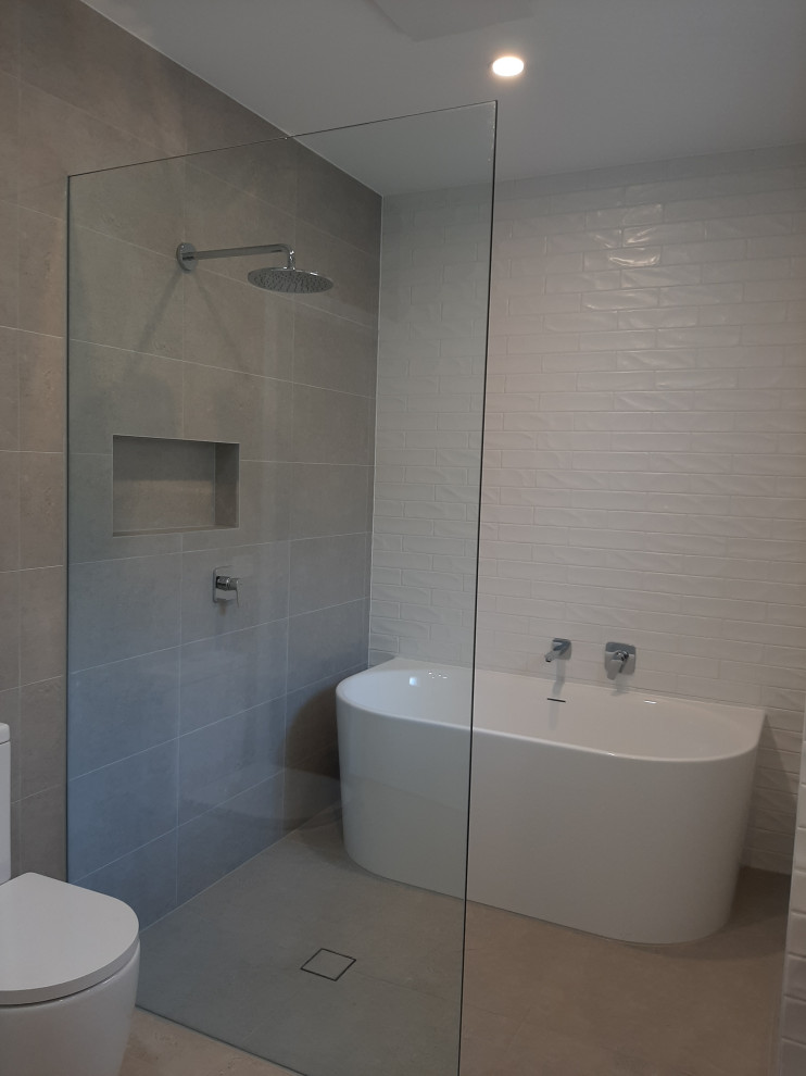 Cette photo montre une grande salle de bain principale moderne en bois brun avec une baignoire indépendante, un carrelage blanc, un plan de toilette en quartz modifié, un sol gris, un plan de toilette blanc, meuble double vasque et meuble-lavabo suspendu.