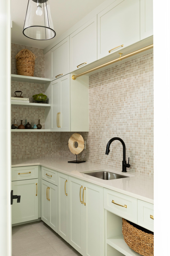 Design ideas for a mid-sized transitional l-shaped dedicated laundry room in Orlando with an undermount sink, shaker cabinets, green cabinets, white walls, ceramic floors, beige splashback, mosaic tile splashback, grey floor and beige benchtop.