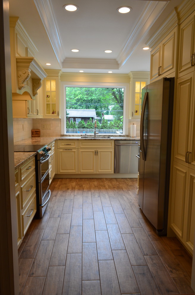 Photo of a mid-sized traditional l-shaped separate kitchen in New York with an undermount sink, raised-panel cabinets, beige cabinets, beige splashback, travertine splashback and stainless steel appliances.
