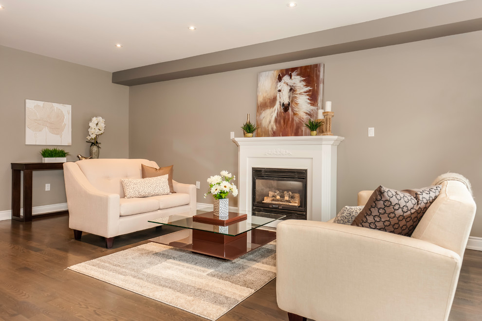 This is an example of a mid-sized transitional open concept family room in Toronto with beige walls, dark hardwood floors, a standard fireplace, a wood fireplace surround, no tv and brown floor.