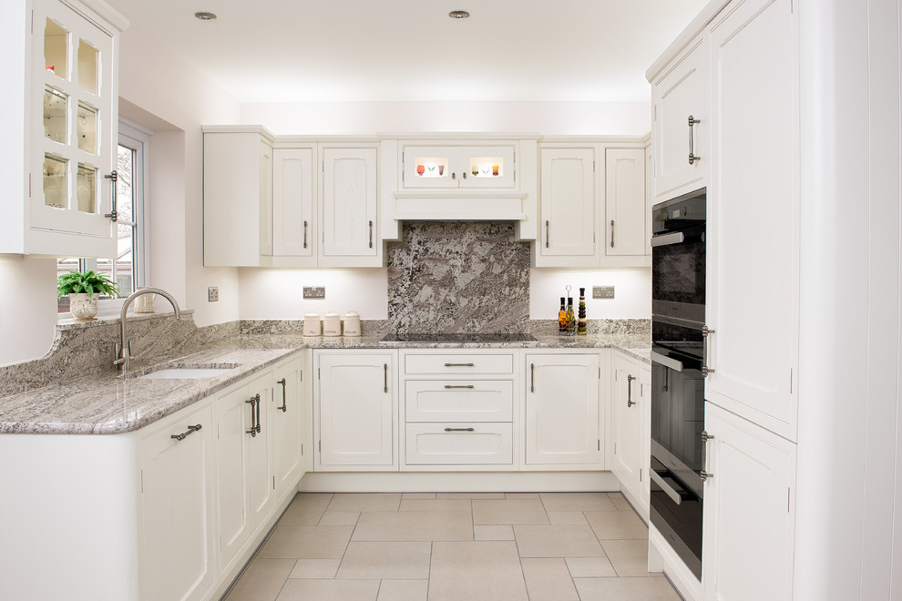 Photo of a mid-sized traditional u-shaped kitchen in Other with an undermount sink, beaded inset cabinets, granite benchtops, stainless steel appliances, white cabinets, grey splashback and stone slab splashback.