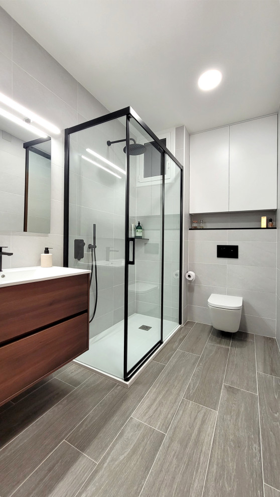 Idéer för att renovera ett litet funkis vit vitt en-suite badrum, med släta luckor, vita skåp, en dusch i en alkov, en vägghängd toalettstol, grå kakel, keramikplattor, grå väggar, klinkergolv i porslin, ett integrerad handfat, kaklad bänkskiva, grått golv och dusch med skjutdörr