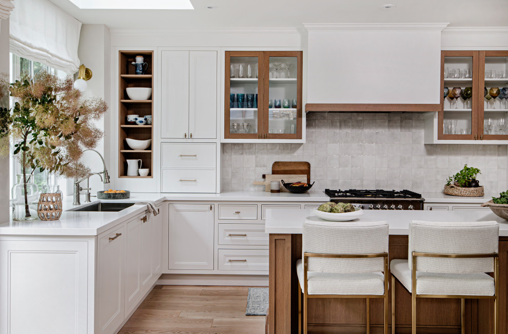 Mid-sized transitional l-shaped open plan kitchen in Toronto with a single-bowl sink, shaker cabinets, white cabinets, solid surface benchtops, yellow splashback, porcelain splashback, panelled appliances, light hardwood floors, with island, brown floor and white benchtop.