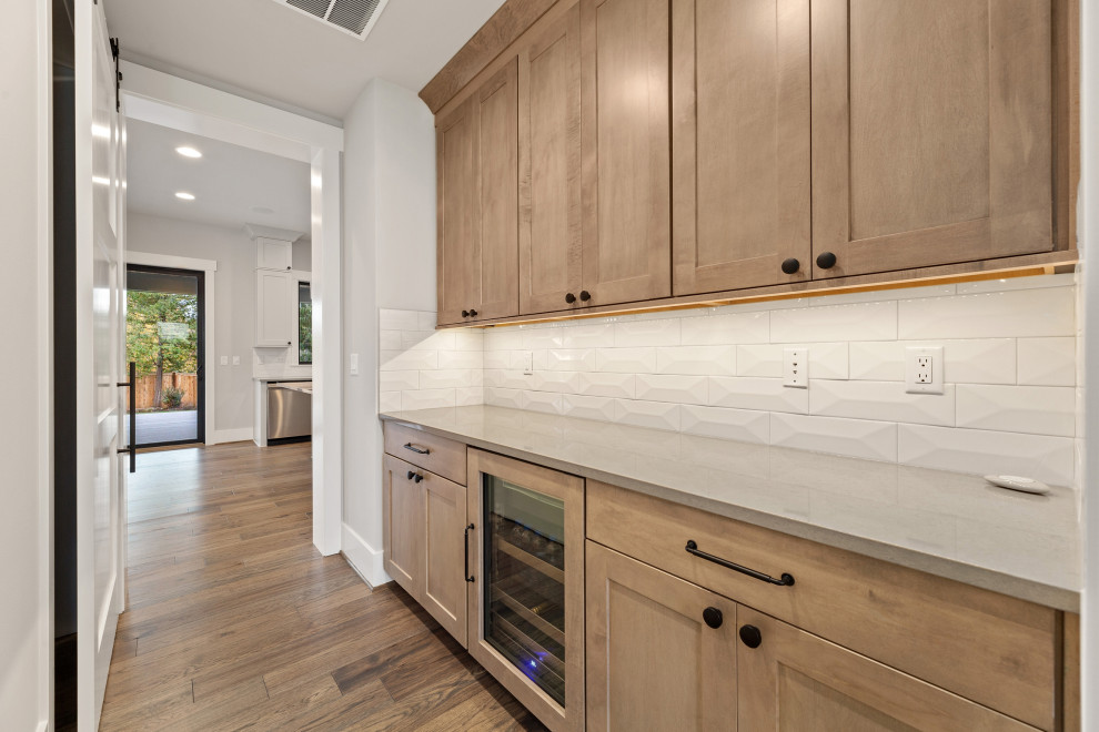 Exempel på ett mellanstort klassiskt grå linjärt grått kök, med luckor med infälld panel, skåp i ljust trä, bänkskiva i kvarts, vitt stänkskydd, stänkskydd i keramik, integrerade vitvaror, mellanmörkt trägolv och brunt golv