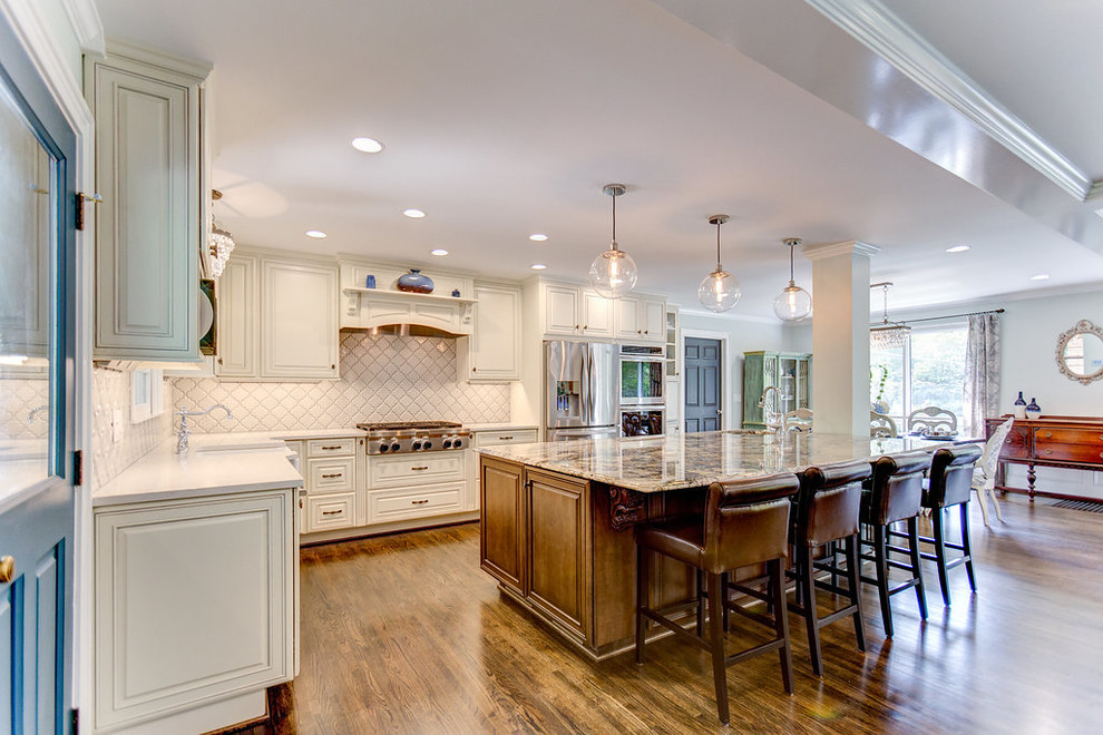 Inspiration for a large l-shaped medium tone wood floor open concept kitchen remodel in Birmingham with a farmhouse sink, raised-panel cabinets, white cabinets, granite countertops, white backsplash, ceramic backsplash, stainless steel appliances and an island