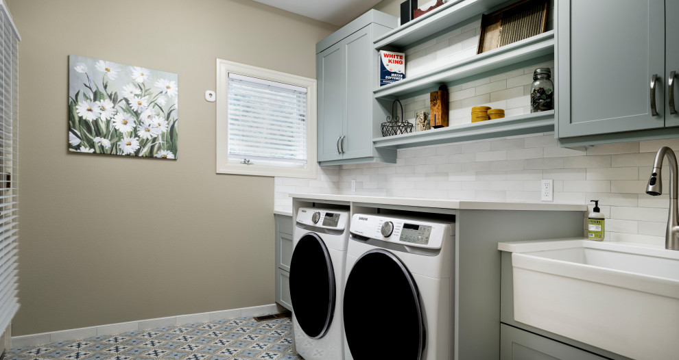 シアトルにある中くらいなコンテンポラリースタイルのおしゃれな洗濯室 (I型、エプロンフロントシンク、シェーカースタイル扉のキャビネット、青いキャビネット、クオーツストーンカウンター、白いキッチンパネル、セラミックタイルのキッチンパネル、ベージュの壁、磁器タイルの床、左右配置の洗濯機・乾燥機、青い床、白いキッチンカウンター) の写真