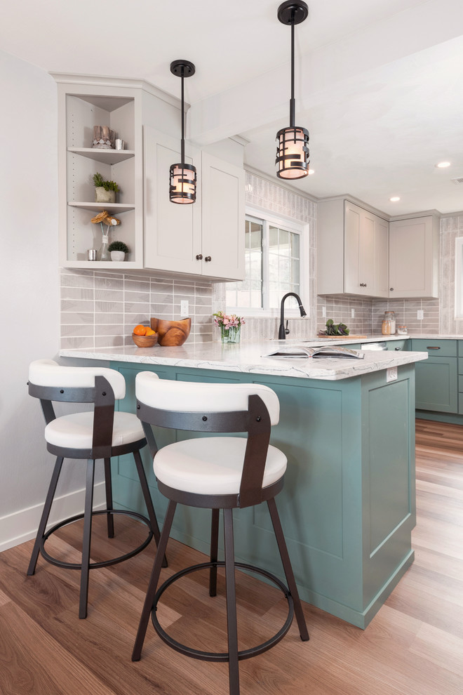 Example of a transitional u-shaped medium tone wood floor and brown floor enclosed kitchen design with an undermount sink, shaker cabinets, turquoise cabinets, quartzite countertops, gray backsplash, porcelain backsplash, stainless steel appliances, a peninsula and white countertops