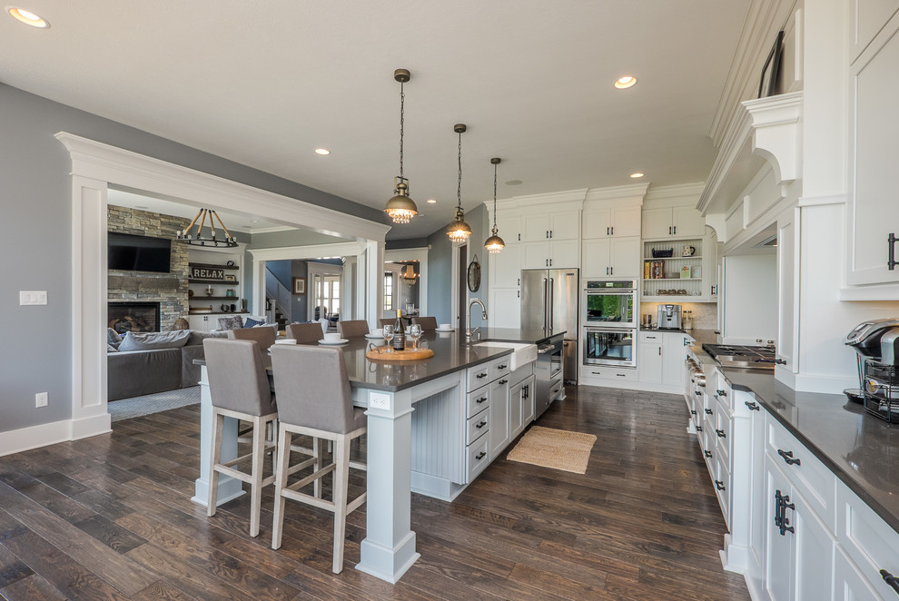 Photo of a traditional kitchen in Other with a farmhouse sink, shaker cabinets, white cabinets, stainless steel appliances, dark hardwood floors and with island.