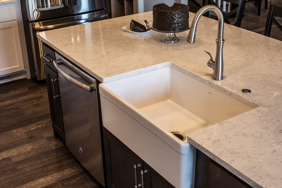Example of a transitional kitchen design with a farmhouse sink, shaker cabinets, white cabinets, quartz countertops, beige backsplash, glass tile backsplash, stainless steel appliances and an island