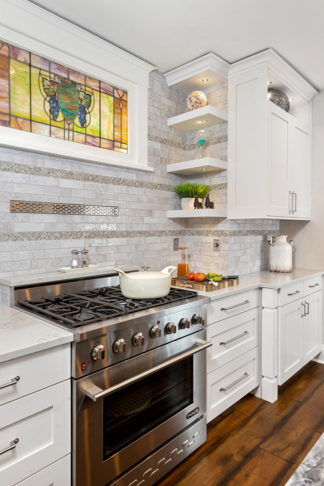 Example of a mid-sized galley medium tone wood floor and brown floor eat-in kitchen design with a single-bowl sink, shaker cabinets, white cabinets, quartz countertops, gray backsplash, subway tile backsplash, stainless steel appliances, an island and white countertops