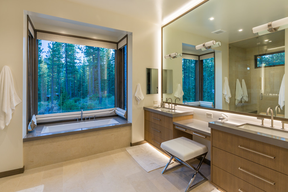 This is an example of a large contemporary master bathroom in Sacramento with flat-panel cabinets, brown cabinets, an undermount tub, a curbless shower, a one-piece toilet, beige tile, travertine, white walls, limestone floors, an undermount sink, engineered quartz benchtops, beige floor and a hinged shower door.