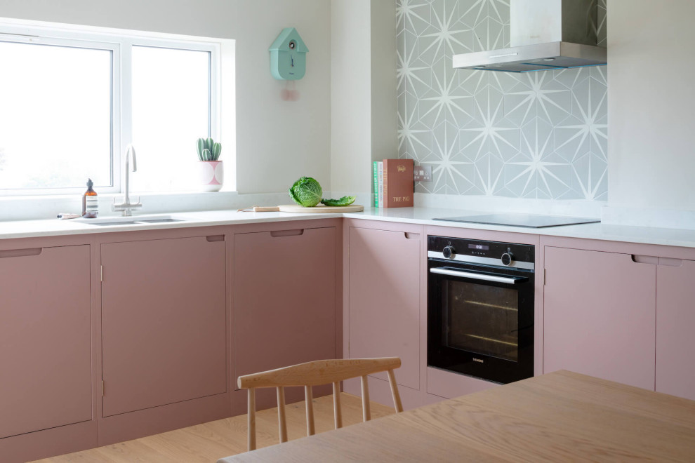 Photo of a mid-sized scandinavian l-shaped eat-in kitchen in Other with flat-panel cabinets, pink cabinets, quartz benchtops, light hardwood floors, no island and white benchtop.