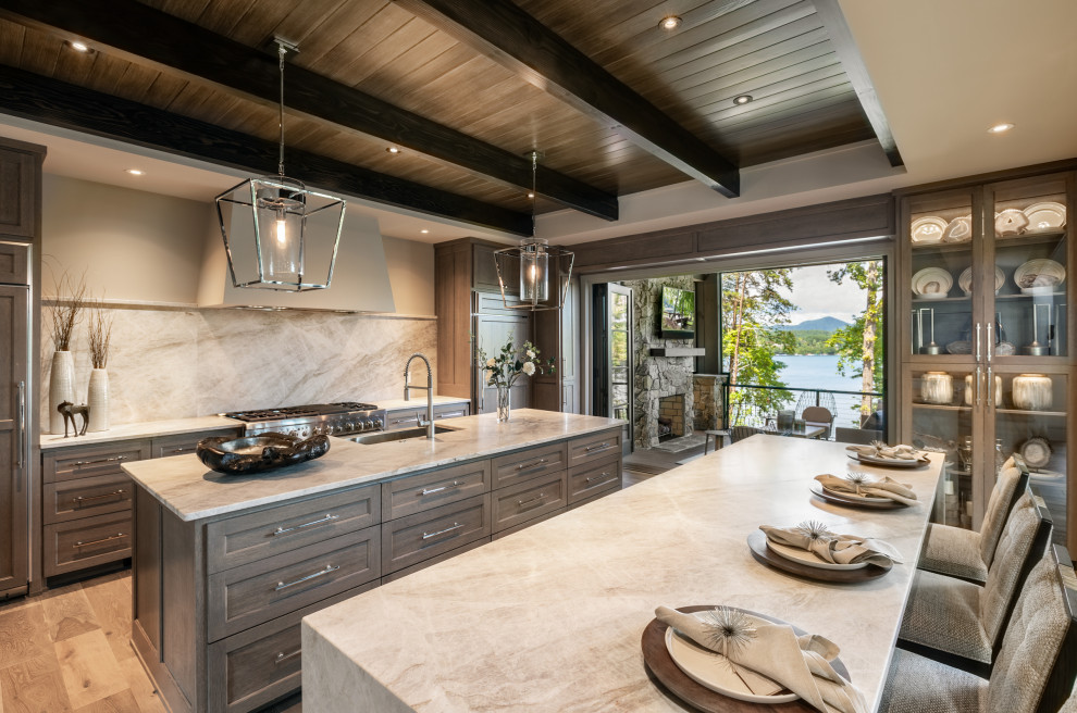 Photo of a country kitchen in Other with a farmhouse sink, shaker cabinets, medium wood cabinets, grey splashback, stone slab splashback, stainless steel appliances, light hardwood floors, multiple islands, beige floor, white benchtop, exposed beam and wood.