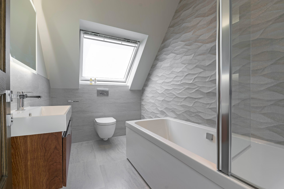 Photo of a mid-sized contemporary bathroom in London with flat-panel cabinets, dark wood cabinets, a corner tub, a wall-mount toilet, grey walls, a wall-mount sink, grey floor and gray tile.