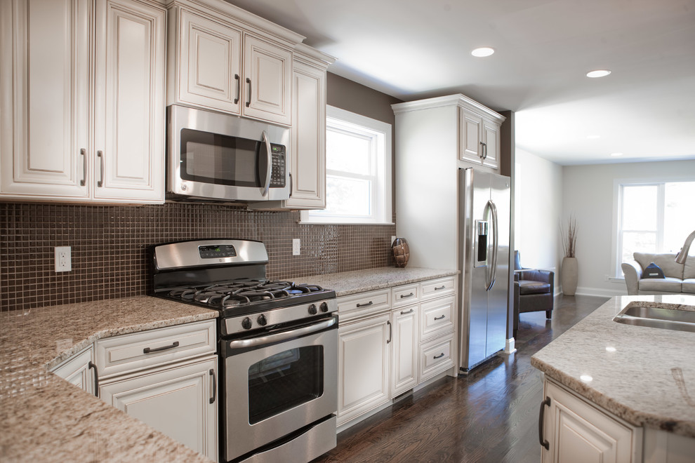 Example of a mid-sized transitional galley dark wood floor kitchen design in St Louis with raised-panel cabinets, white cabinets, granite countertops, brown backsplash, mosaic tile backsplash, stainless steel appliances and an island