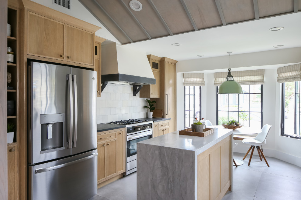 Beach style eat-in kitchen in Orange County with light wood cabinets, marble benchtops, a farmhouse sink, stainless steel appliances, ceramic floors, with island, grey floor and marble splashback.