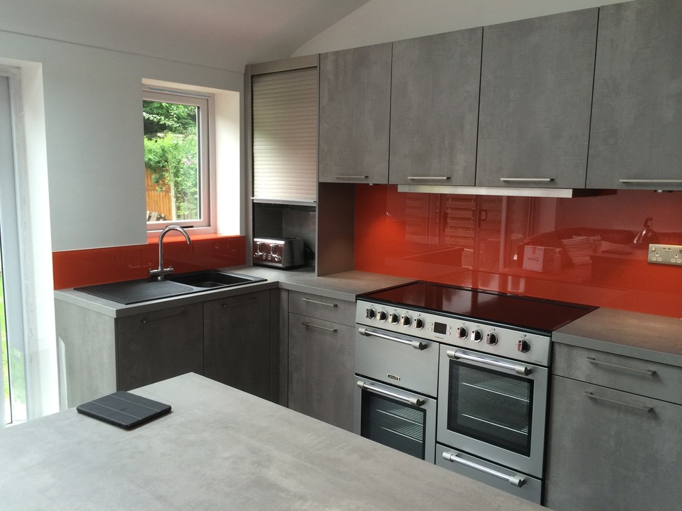 Photo of a mid-sized industrial l-shaped open plan kitchen in Cheshire with glass sheet splashback, no island, grey cabinets and orange splashback.